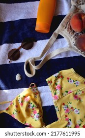 Striped Towel, Yellow Floral Swimming Suit, Sunglasses, Mesh Tote With Fresh Peaches, Seashell And Sunscreen. Beach Essentials, Flat Lay.