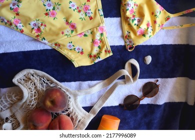 Striped Towel, Yellow Floral Swimming Suit, Sunglasses, Mesh Tote With Fresh Peaches, Seashell And Sunscreen. Beach Essentials, Flat Lay.