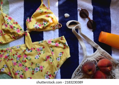 Striped Towel, Yellow Floral Swimming Suit, Sunglasses, Mesh Tote With Fresh Peaches, Seashell And Sunscreen. Beach Essentials, Flat Lay.