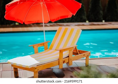 Tumbona de playa de verano despojada con paraguas rojos contra piscina azul. Día soleado. No hay gente