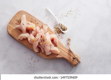 Strips Of Lean Healthy Uncooked Chicken Breast Sprinkled With A Savory Spice Mix Heaped On A Wooden Board Ready For Cooking In A Top Down View On White Marble