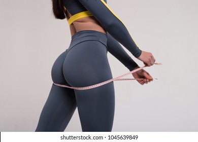 Strive for progress, not perfection. Closeup of fitness woman with tight hips and firm buttocks in workout leggings and measuring tape.