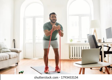 Strive for strong body. Full length shot of young active man showing exercises with resistance band, streaming video lesson on training at home using laptop. Sport online concept. Horizontal shot - Powered by Shutterstock