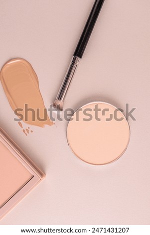 A stroke of foundation, a round block of compact powder, a makeup brush on a beige background. The top vertical view. The concept of beauty, makeup