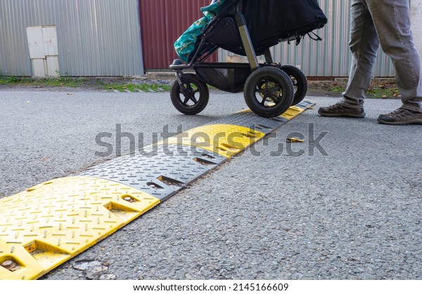 Stroller crossing speed bump on the road, yellow and\
black striped speed bump in asphalt road to slow down fast moving\
cars