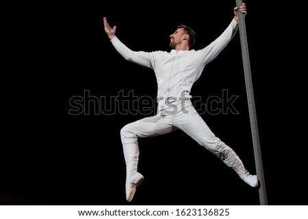 strong acrobat posing while performing and holding metallic pole isolated on black
