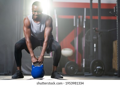 Strong adult black African men swing kettlebell to do crossfit exercise and weight lifting inside of fitness gym to workout for body strength and firm arms muscle and good physical body health.  - Powered by Shutterstock