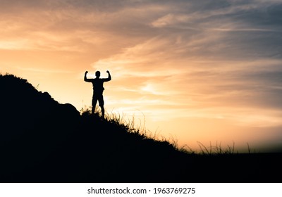 Strong Adventurous Man Standing On On A Mountain Flexing His Arms Top To The Sky. Never Give Up, And Sport Adventure Concept. 