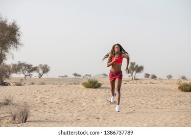 Strong African Black Woman With Long Braids In Hair In The Desert Wearing Red Sportswear Runs Toward The Camera   