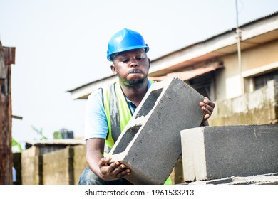 
Strong African male construction worker effortlessly working and carrying bricks on building site and wearing a blue safety helmet known as hardhat and green reflective traffic jacket