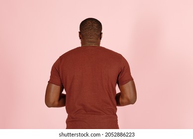 Strong African-American Man Actor In Brown T-shirt Poses For Camera On Pink Background In Studio Back View