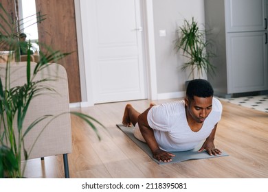 Strong African-American Man Practicing Burpee Exercise At Home, Doing Push-ups And Jumping On Yoga Mat At Bright Domestic Room. Concept Of Sport Training At Home Gym.