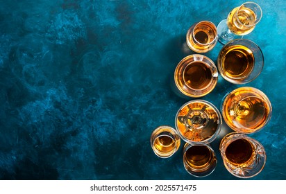 Strong alcohol drinks, hard liquors, spirits and distillates iset in glasses: cognac, scotch, whiskey and other. Blue background, top view 
