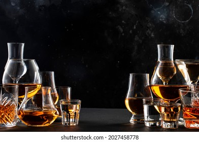 Strong alcohol drinks, hard liquors, spirits and distillates iset in glasses: cognac, scotch, whiskey and other. Black bar counter background