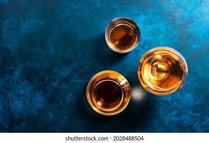 Strong alcohol drinks, hard liquors, spirits and distillates set in glasses: cognac, scotch, whiskey and other. Blue background, top view 