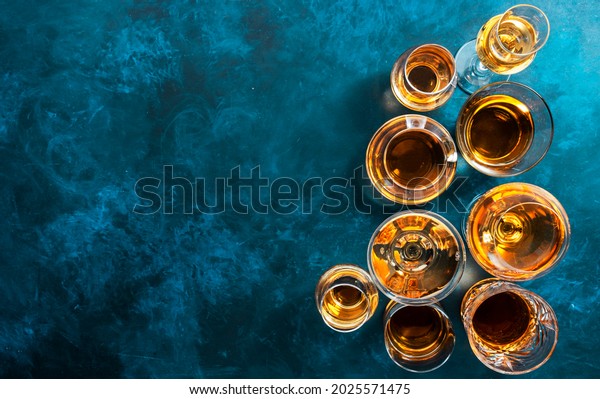 Strong alcohol drinks, hard liquors, spirits and\
distillates iset in glasses: cognac, scotch, whiskey and other.\
Blue background, top view\

