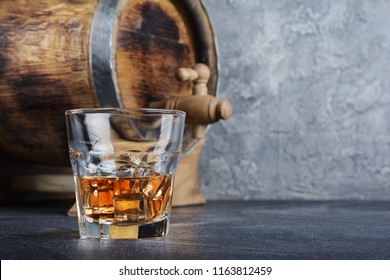 Strong Alcoholic Drink Scotch Whisky With Ice Cubes In Old Fashion Glass And Vintage Wooden Barrel In Cellar On Gray Concrete Background