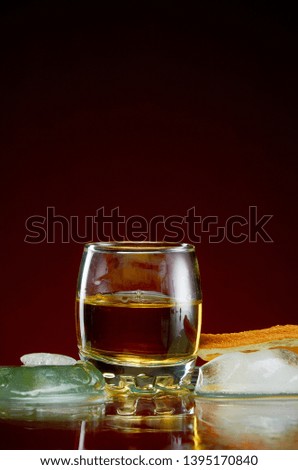 Strong alcoholic drink in a transparent glass with ice on a red background