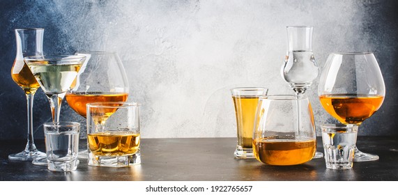 Strong alcoholic drinks in glasses in assortment: vodka, cognac, tequila, brandy and whiskey, grappa, liqueur, vermouth, tincture, rum. Gray bar counter with copy space