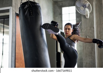 Strong Asian boxing woman jump kick to huge punching bag at fitness gym. Athletic girl training Muay Thai boxing for bodybuilding and healthy lifestyle concept. workout in sport club.