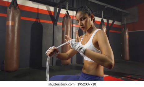 Strong Asian woman doing hand wrapping with a rope, combat punches in boxing sport club workout at training gym fitness center. Exercise indoor sport equipment. People lifestyle. - Powered by Shutterstock