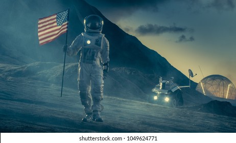 Strong Astronaut On Alien Planet Walks Through the Storm with a Flag of Unites States of America. In the Background His Research Base/ Station and Rover. Space Travel, Colonisation Theme. - Powered by Shutterstock