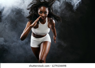 Strong Athletic Black Skin Woman Sprinter, Running On Background With Smoke Wearing In The Sportswear. Fitness And Sport Motivation. Runner Concept With Copy Space.