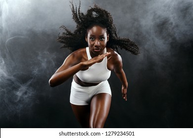 Strong Athletic Black Skin Woman Sprinter, Running On Background With Smoke Wearing In The Sportswear. Fitness And Sport Motivation. Runner Concept With Copy Space.