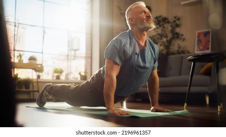 Strong Athletic Fit Senior Man Training on a Yoga Mat, Doing Back Stretching and Core Strengthening Exercises During Morning Workout at Home in Sunny Apartment. Concept of Health and Fitness. - Powered by Shutterstock