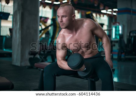 Strong athletic man make exercise with the dumbbells in the gym.