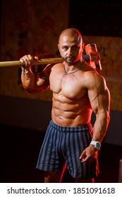 Strong athletic man posing with a sports hammer on the background of the gym. A strong bodybuilder with perfect abs, shoulders, biceps, triceps and chest.