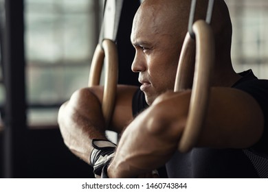 Strong athletic man resting on gymnastic rings. Black guy take a break at gym holding dip ring. Fit african man athlete training on gymnastic rings.  - Powered by Shutterstock