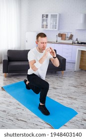A strong athletic man in a T-shirt does exercises in his spacious apartment with a minimalistic interior. Healthy lifestyle during the quarantine period. Fitness at home