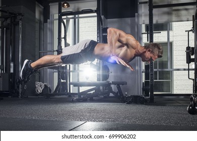 Strong Athletic Muscular White Man Does Plyometric Pushup In A Dark Gym With A Light Flare 