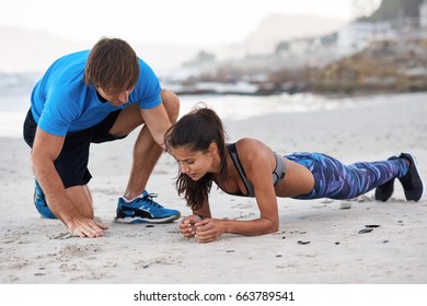 Strong athletic woman planking on beach while personal trainer coach motivates and corrects her posture form - Powered by Shutterstock