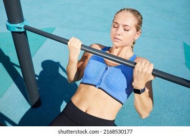 Strong attractive young woman in sports bra gripping bar while performing Australian pull-ups at sports ground - Powered by Shutterstock