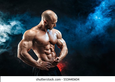 Strong bald bodybuilder with six pack. Bodybuilder man with perfect abs, shoulders,biceps, triceps and chest, personal fitness trainer flexing his muscles in blue, red smoke