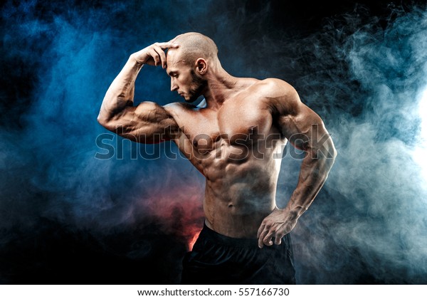 6つのパックを持つ丈夫な禿げたボディビルダー ボディビルダーの男性で 完璧な腹筋 肩 二頭筋 三頭筋 胸 パーソナルフィットネストレーナーが 青い赤い煙で筋肉を曲げる の写真素材 今すぐ編集