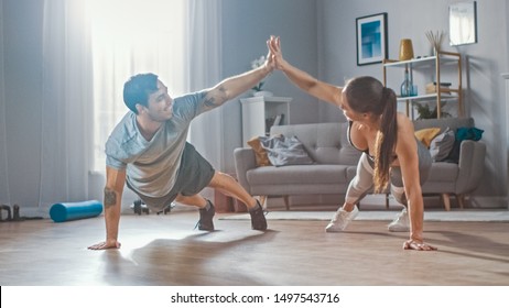 Strong and Beautiful Athletic Fitness Couple in Workout Clothes Doing Push Up Exercises and Giving Each Other a High Five in Their Bright and Spacious Living Room with Minimalistic Interior.