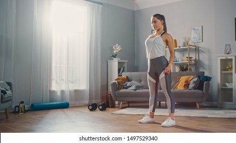 Strong and Beautiful Athletic Fitness Girl in Sportswear is Standing in Her Bright and Spacious Living Room with Minimalistic Interior.