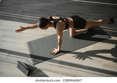 Strong Beautiful Fitness Girl in Workout Clothes Does Stretching Yoga Exercises at gym, Uses Digital Tablet for Online Exercise, Workout, Streaming Fitness - Powered by Shutterstock