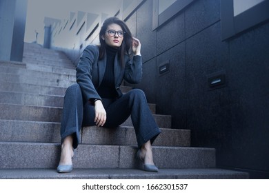 Strong Beautiful Young Woman In A Bussines Suit And Glasses Siting On The Office Steps