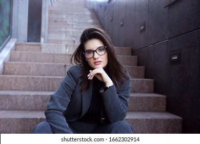 Strong Beautiful Young Woman In A Bussines Suit And Glasses Siting On The Office Steps