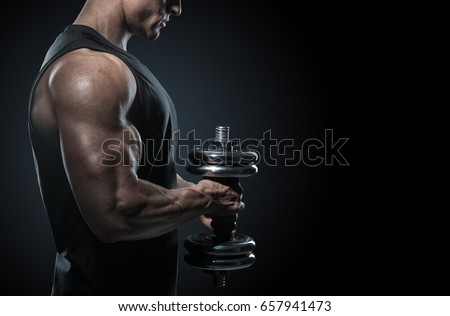 Strong bodybuilder with perfect deltoid muscles, shoulders, biceps, triceps and chest. Close-up of a power fitness man. Handsome power athletic man in training pumping up muscles with dumbbell.