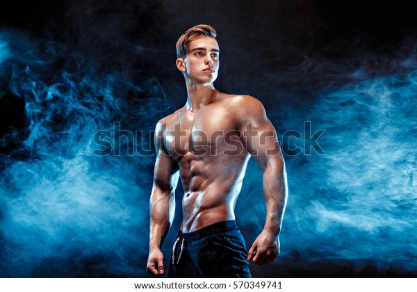 6つのパック 完璧な腹筋 肩 二頭筋 三頭筋 胸 パーソナルフィットネストレーナーが煙の中で筋肉を曲げている強力なボディビルダー の写真素材 今すぐ編集