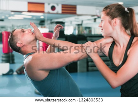 Strong bold positive cheerful  woman is training with man on the self-defense course in gym.