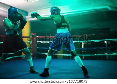 Strong boxer girls fighting for victory on ring. Two Caucasian girls in helmets and gloves boxing in gym, attacking each other doing their best, trying to win. Combat sport and womens boxing concept