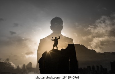 Strong Brave Man Showing No Fear Climbing To The Top Of A Mounting Facing The City. People Mental Strength And Motivation Concept. 