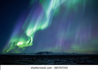 Strong bright purple green aurora noprthern lights over mountain lava plain, Thingvellir, Iceland