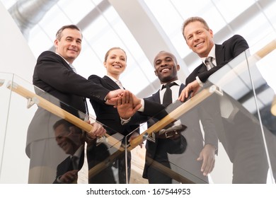 Strong Business Team. Low Angle View Of Four Confident Business People Standing Close To Each Other And Holding Hands Together